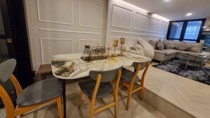 A modern dining area with a marble table, wooden chairs, and a sofa in the background. - Oliver's House in Kaset (Bangkok)