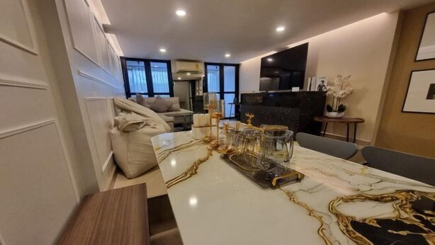 A modern kitchen with a marble countertop, a dining area with a white table, and a sofa. - Oliver's House in Kaset (Bangkok)
