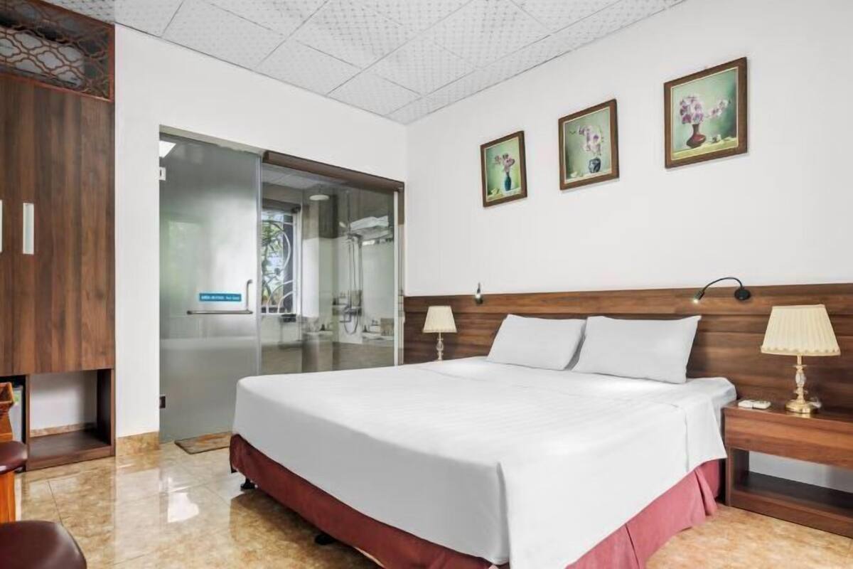A hotel room with a bed, a nightstand, a desk, a chair, and a sliding glass door leading to a bathroom.