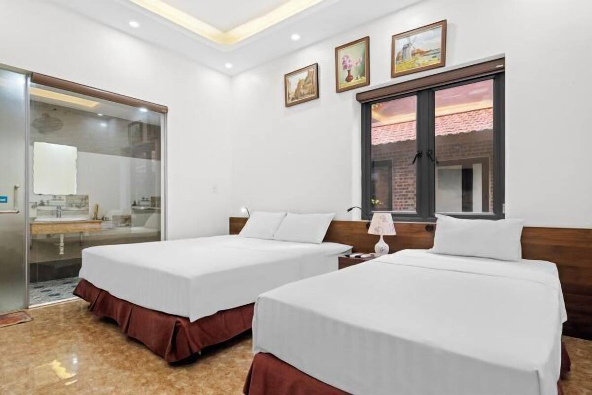 A hotel room with two beds, a window with a view, a mirror, and a door leading to a bathroom.