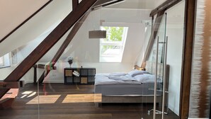 Ein modernes Schlafzimmer im Loft-Stil mit schrägem Dach, einer Glastür zum Verschieben, einem Bett mit weißer Bettwäsche und Holzboden.