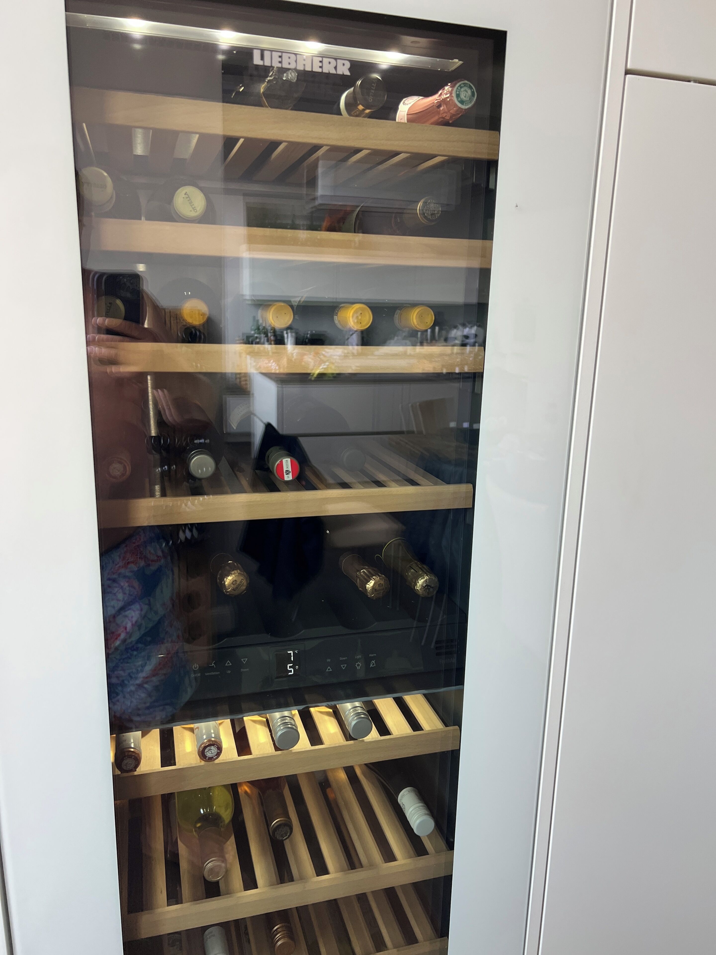 Un réfrigérateur à vin doté de plusieurs étagères, d’un affichage numérique de la température et d’une bouteille de vin placée sur l’étagère inférieure.