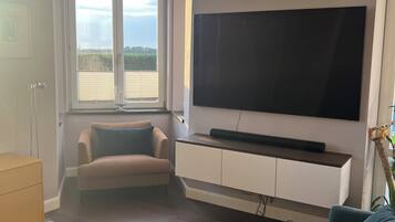 Sala de estar com uma TV de tela plana grande fixada na parede, um sofá bege, um sofá azul e piso de madeira.