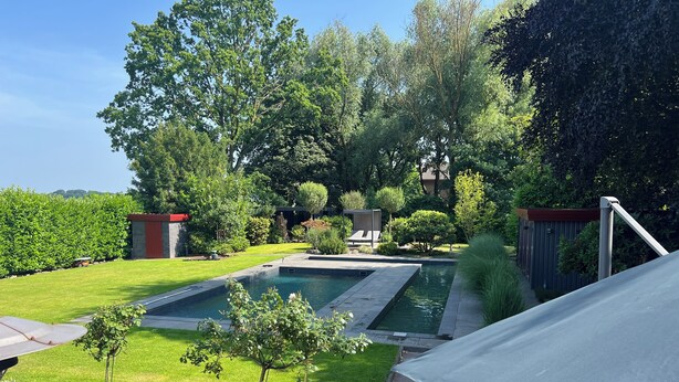 Ein Garten mit einem rechteckigen Pool, einer Holzterrasse und einem überdachten Sitzbereich.