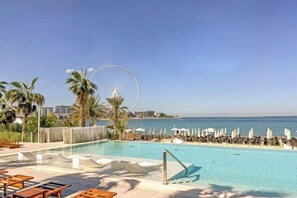 Un espace piscine avec des chaises longues et des parasols, une grande roue en arrière-plan et une vue dégagée sur la mer.