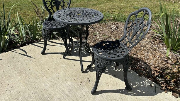 Un patio con una mesa redonda y dos sillas, rodeado de plantas y un área con césped.