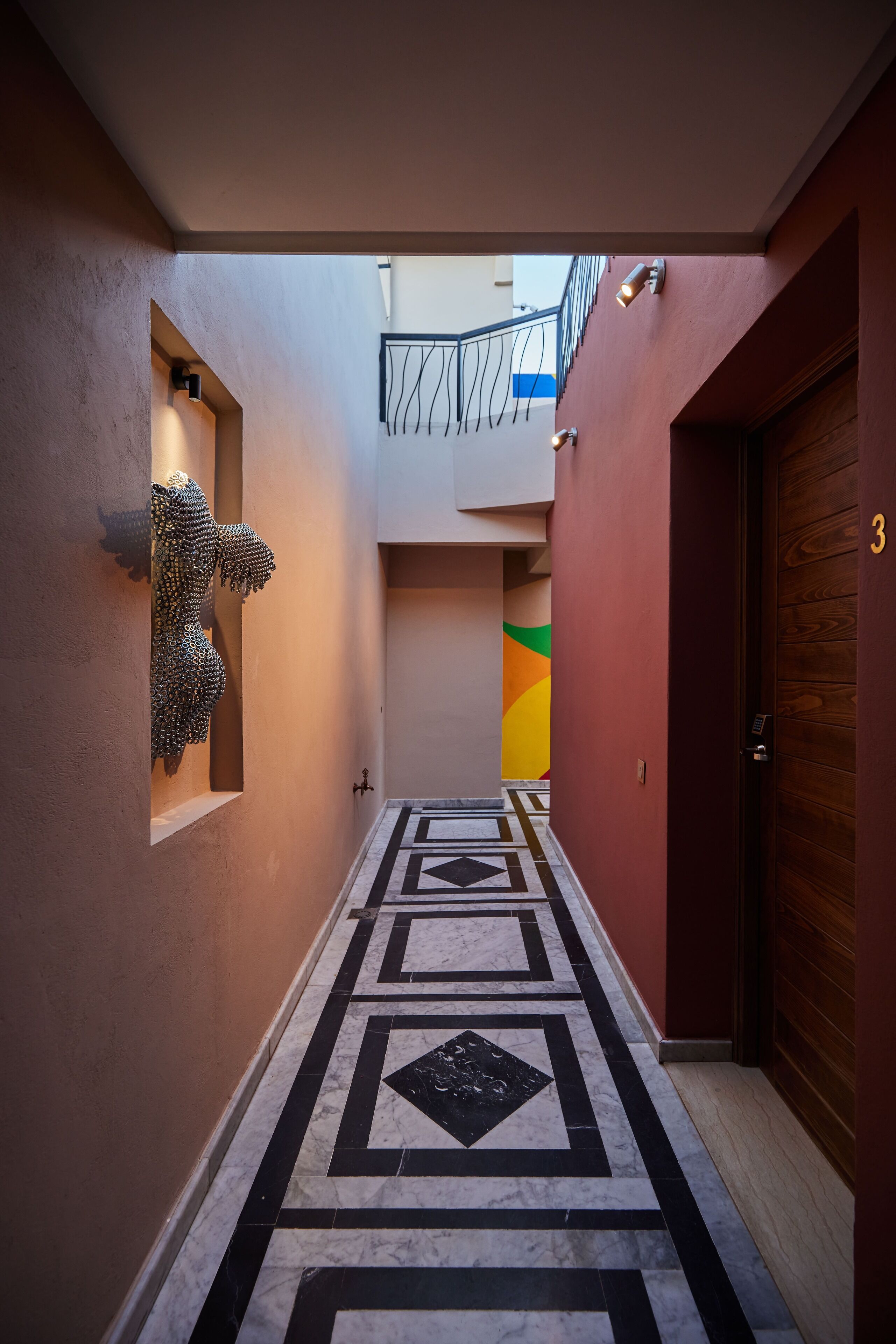A hallway with a geometric patterned floor, a wooden door with the number 3, and a wall-mounted sculpture.