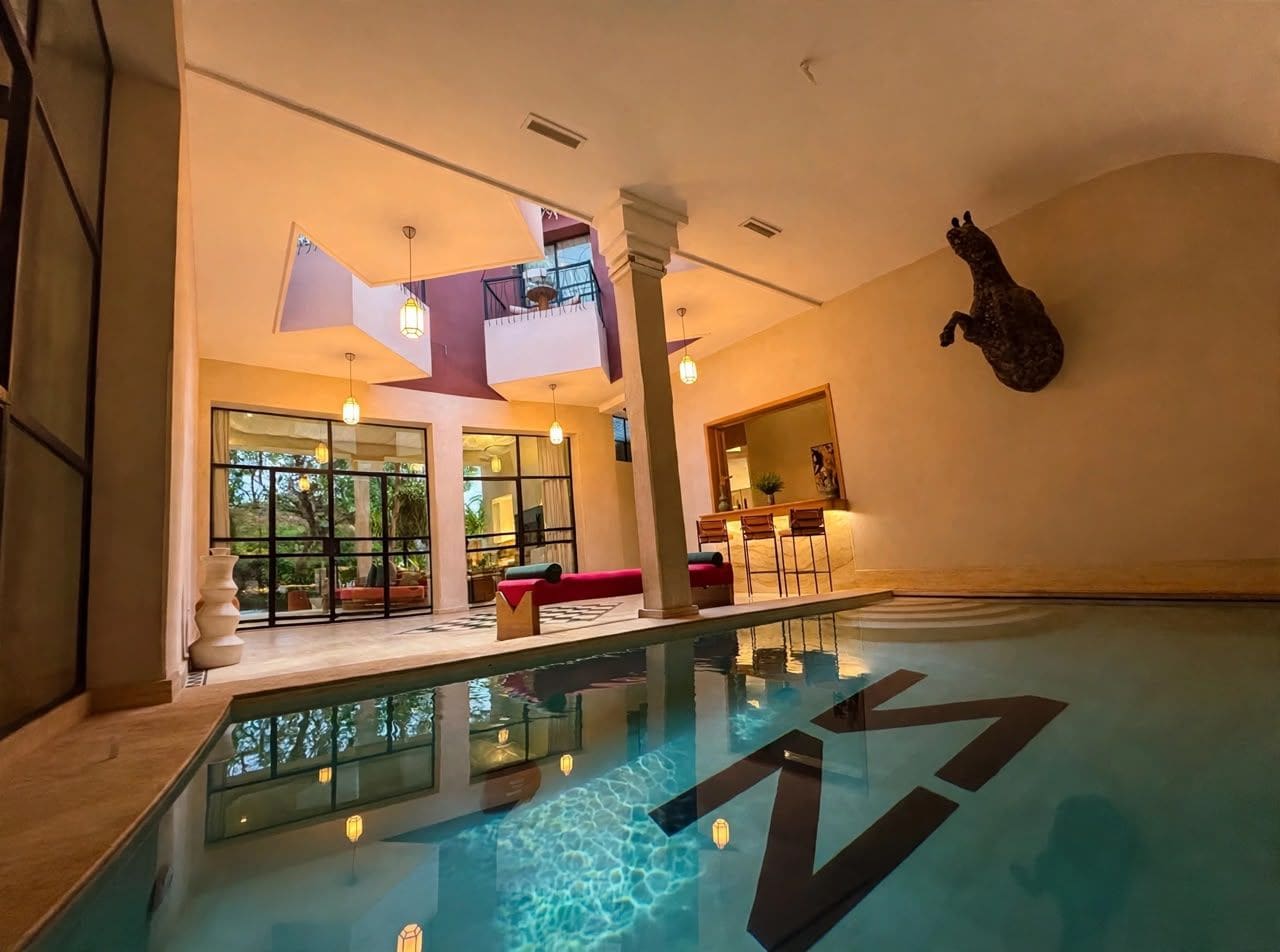 Una piscina interior con agua cristalina, un sofá rojo y una zona de bar con sillas.