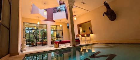 An indoor swimming pool with clear water, a red sofa, and a bar area with chairs.
