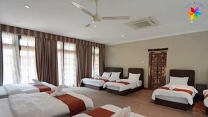 A hotel room with four beds, a ceiling fan, and a large window with curtains.