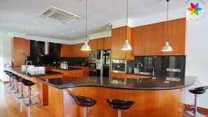 A modern kitchen with a central island, bar stools, stainless steel appliances, and pendant lighting.