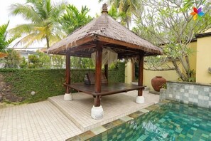 Ein hölzerner Pavillon mit einem Reetdach neben einem Schwimmbecken.