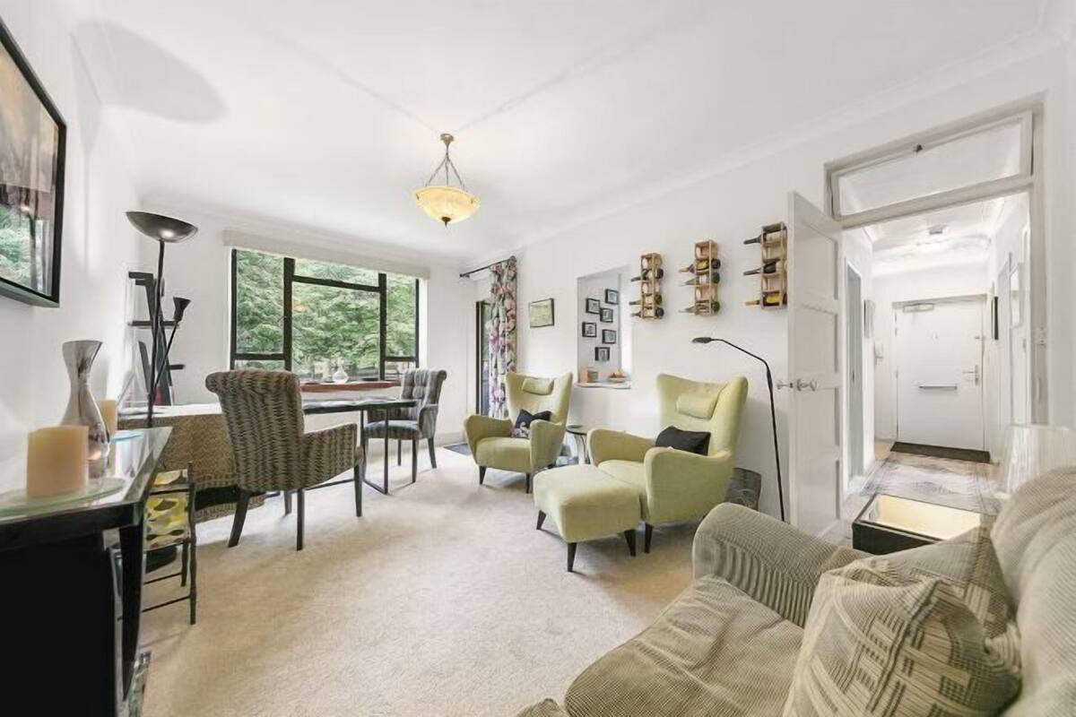 Un salon spacieux comprenant un coin repas, de grandes fenêtres et une vue sur la verdure environnante.