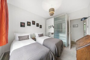 Een slaapkamer met twee bedden, een kledingkast, een bureau en een hanglamp.