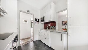 Une cuisine moderne avec des meubles blancs, un four à micro-ondes et un réfrigérateur. On y trouve également un petit îlot central doté d’un évier et d’un plan de travail.