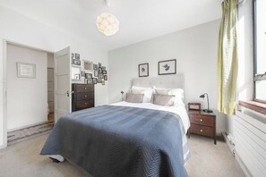 Een slaapkamer met een bed, nachtkastje, lamp en wanddecoratie.