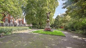 Un parc avec une statue, un chemin pavé et un bâtiment en arrière-plan.