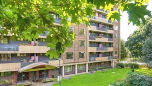 Un immeuble résidentiel à plusieurs étages, doté de balcons, d’une entrée couverte et d’une pelouse bien entretenue.