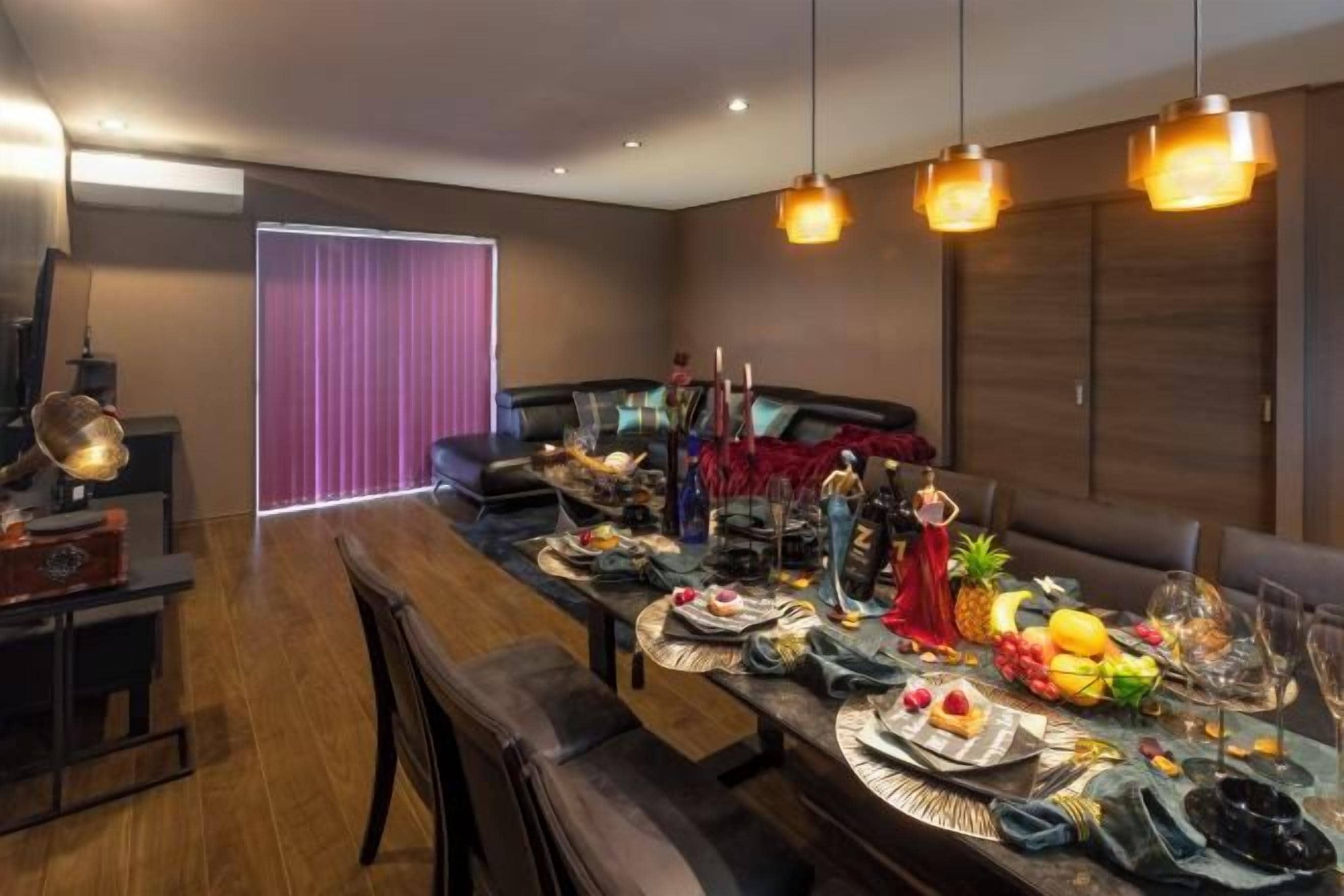 A dining area with a long table set for a meal, a sofa, and a television in the background.