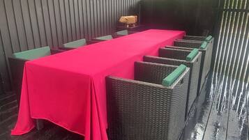 A covered outdoor seating area with a long table and wicker chairs.