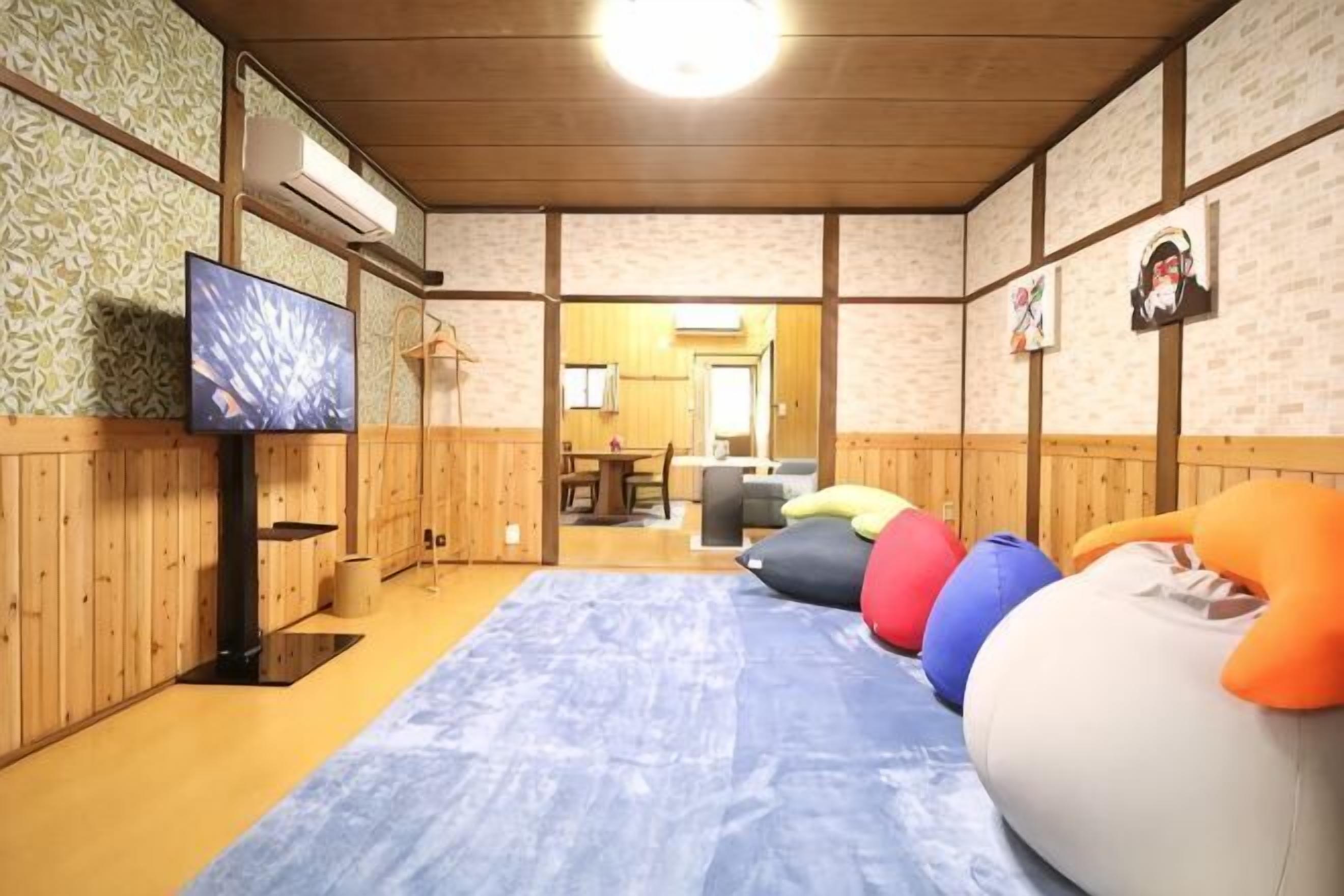 Ein Zimmer mit Tatami-Böden, einem Fernseher, Sitzsäcken, einer Holzbalkendecke und traditioneller japanischer Gestaltung.