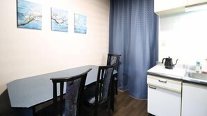 A compact kitchen with a dining table and chairs, a white cabinet, and a window with a curtain. - Ideal Momodani (Osaka)