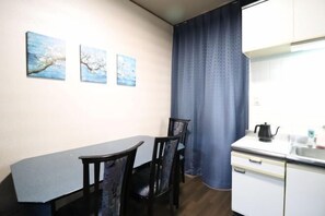 A compact kitchen with a dining table and chairs, a white cabinet, and a window with a curtain. - Ideal Momodani (Osaka)