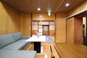 A room with a wooden floor, a sofa, a table with a white top, and a sliding door. - Ideal Momodani (Osaka)