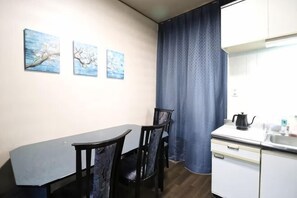 A small, modern kitchen with a dining table and chairs, a white countertop, and a window with a blue curtain. - Ideal momodani (Osaka)