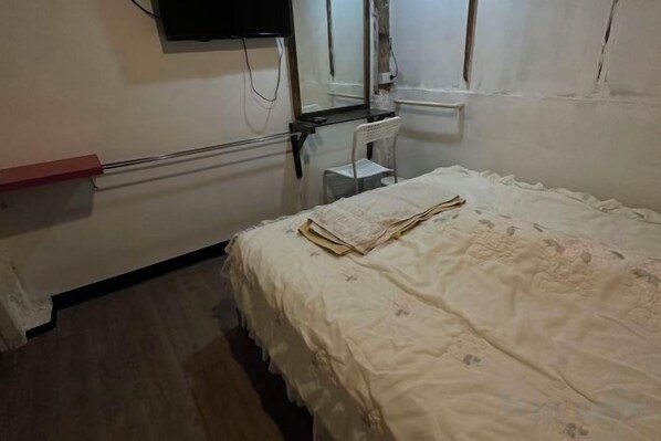 A single bed with a white bedspread, a bedside table, and a wall-mounted television.