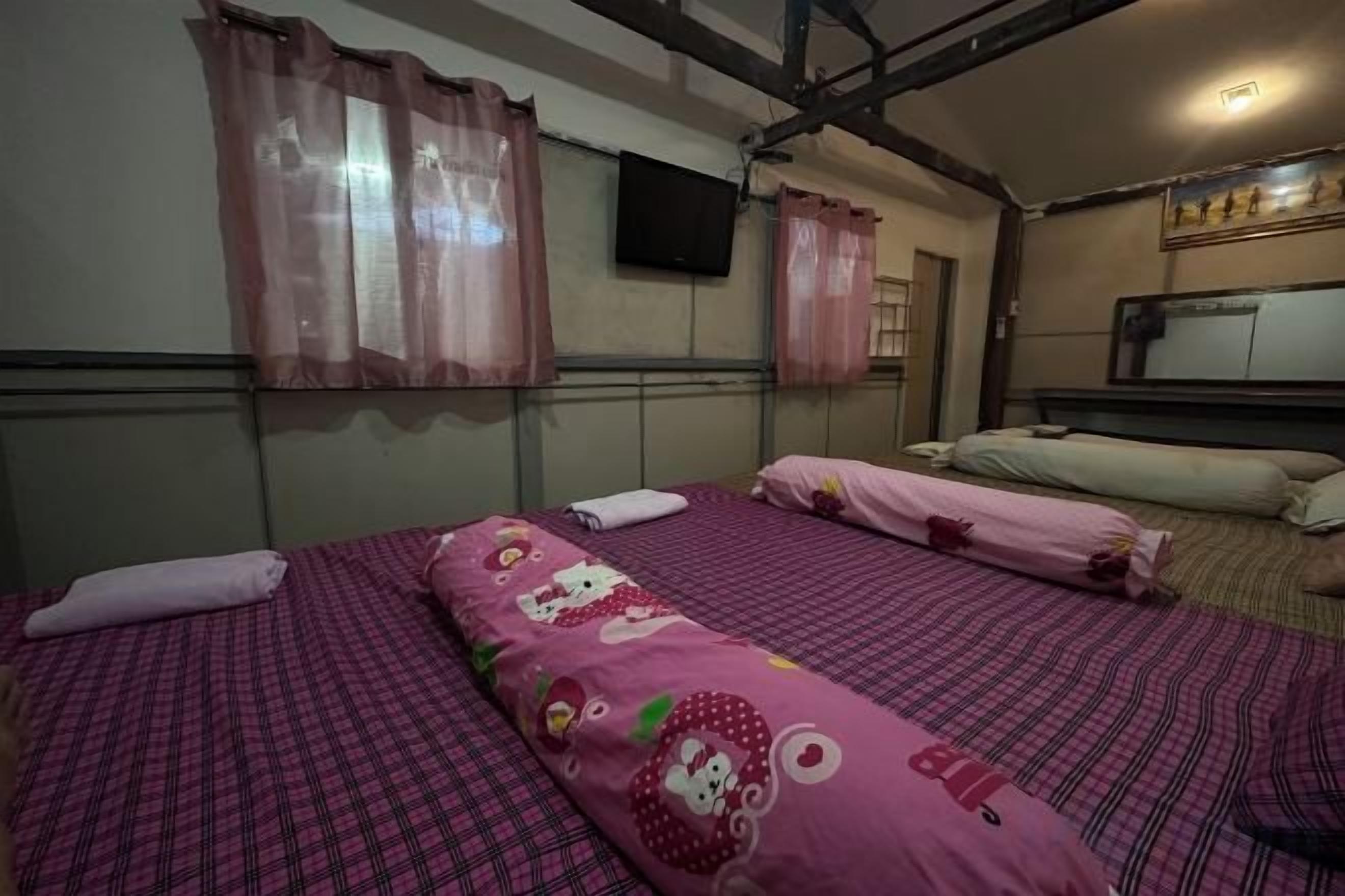 A room with two beds, each with pink bedding and a Hello Kitty design. There is a television on the wall and a window with curtains.