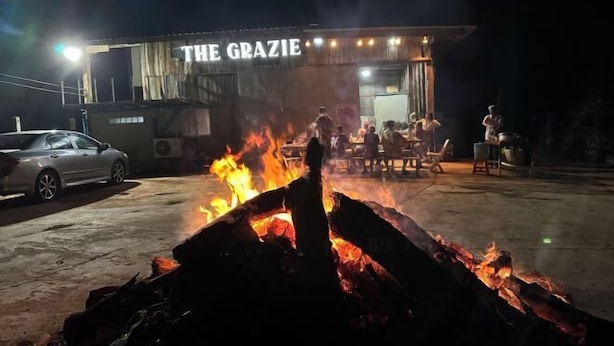 A building with a sign reading "THE GRAZIE" at night, with a fire in the foreground and a car parked outside. - BanGoDangtia (Pak Chong)