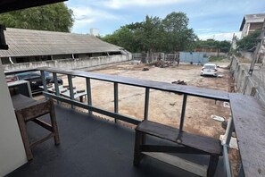 A balcony with a view of a fenced yard, a car, and a building with a corrugated metal roof.