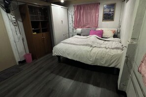 A bedroom with a bed, a wardrobe, a pink curtain, and a wall-mounted fan.