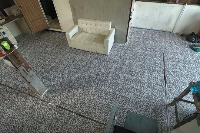 Quarto com ladrilhos no chão, sofá branco e escada de madeira.