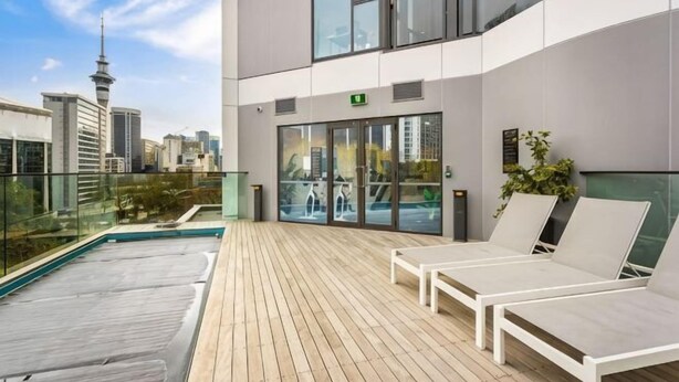 A rooftop terrace with lounge chairs, a pool, and a city view. - Sunny Retreat in Heart of CBD (Auckland)