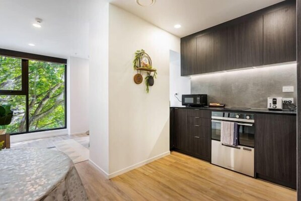 A modern kitchen with dark cabinetry, a built-in oven, and a microwave. - Sunny Retreat in Heart of CBD (Auckland)