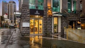 A hotel with a stone facade, a glass entrance, and a visible signboard. - Sunny Retreat in Heart of CBD (Auckland)