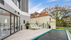 A modern building with a swimming pool, lounge chairs, and a glass door entrance. - Sunny Retreat in Heart of CBD (Auckland)