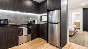 A modern kitchen with dark cabinetry, a stainless steel refrigerator, a built-in oven, and a microwave. - Sunny Retreat in Heart of CBD (Auckland)