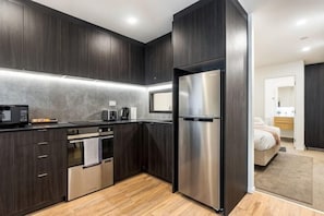 A modern kitchen with dark cabinetry, a stainless steel refrigerator, a built-in oven, and a microwave. - Sunny Retreat in Heart of CBD (Auckland)