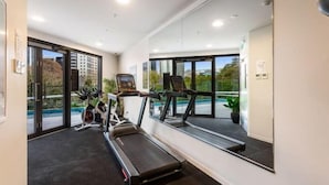 A gym with treadmills, an elliptical, and a stationary bike, large windows, and a view of the outdoors. - Sunny Retreat in Heart of CBD (Auckland)
