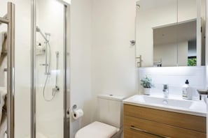 A modern bathroom with a glass shower enclosure, a toilet, a sink with a mirror, and wooden cabinetry. - Sunny Retreat in Heart of CBD (Auckland)