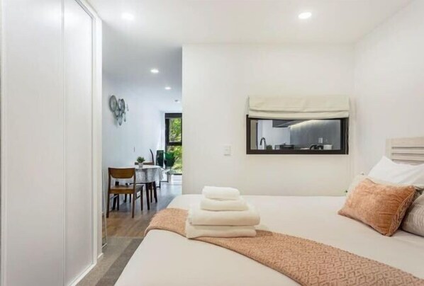 A modern bedroom with a bed, a bedside table, a mirror, and a view of a dining area. - Sunny Retreat in Heart of CBD (Auckland)