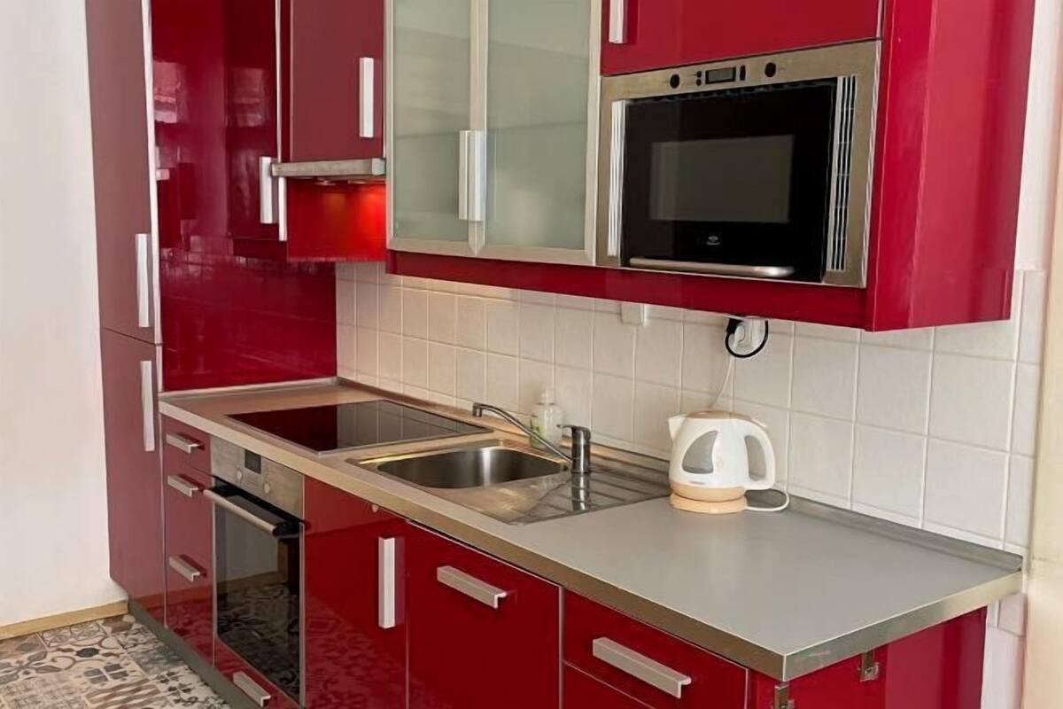 A kitchen with red cabinets, a stainless steel sink, and a built-in oven.