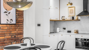 Een moderne keuken met witte kasten, een bakstenen muur, een ronde eettafel en een hanglamp.