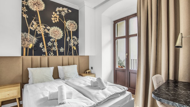 Een hotelkamer met een groot bed, een hoofdbord, een bloemen schilderij, een raam met gordijnen en een klein tafeltje met een lamp.