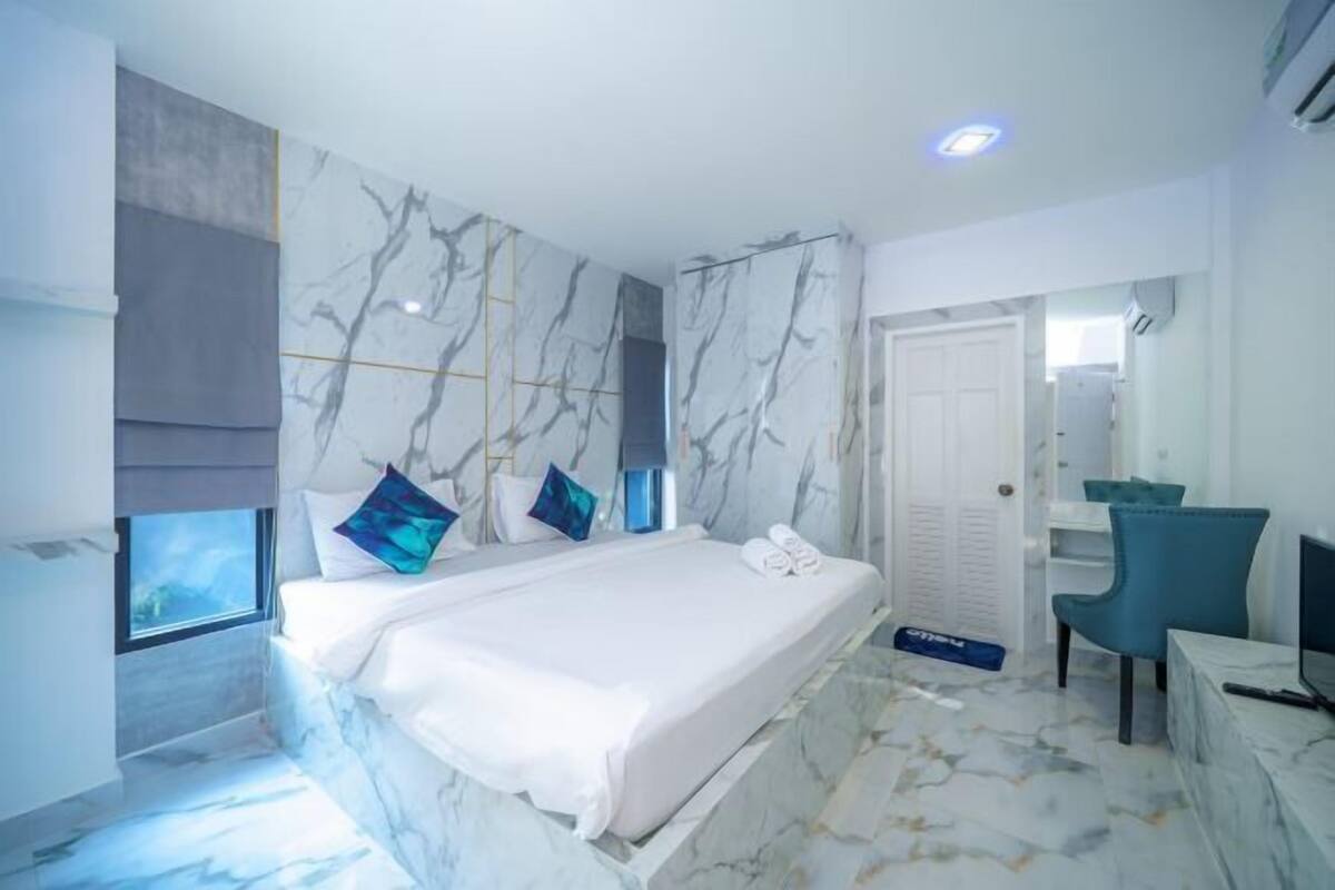 Une chambre moderne avec un mur à motifs de marbre, un lit recouvert de linge de maison blanc et une chaise bleue.