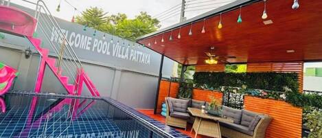 A modern outdoor pool area with a lounge seating arrangement, a staircase, and a wall with a welcoming message.