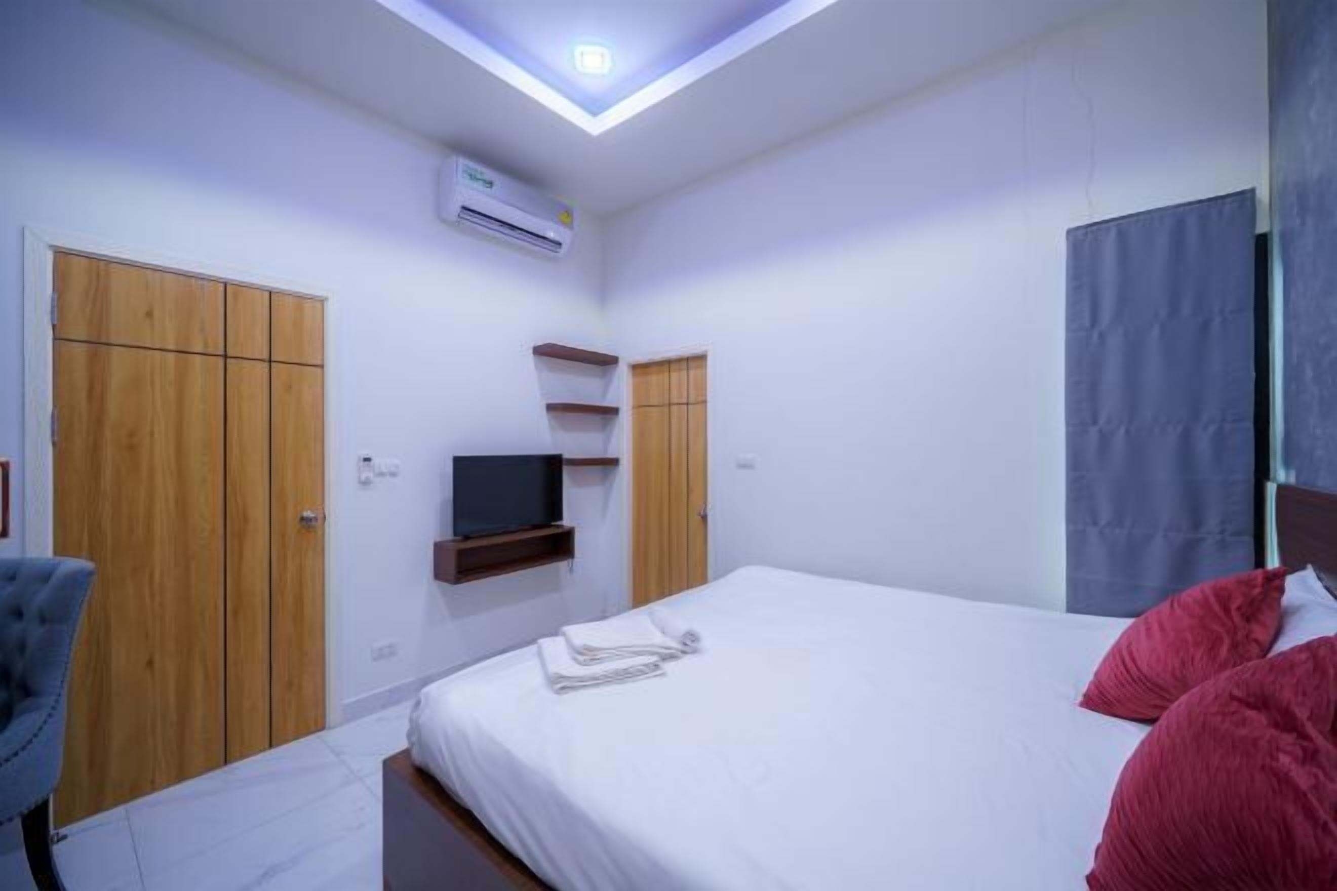 A bedroom with a bed, a TV on a shelf, wooden wardrobes, and a ceiling light.